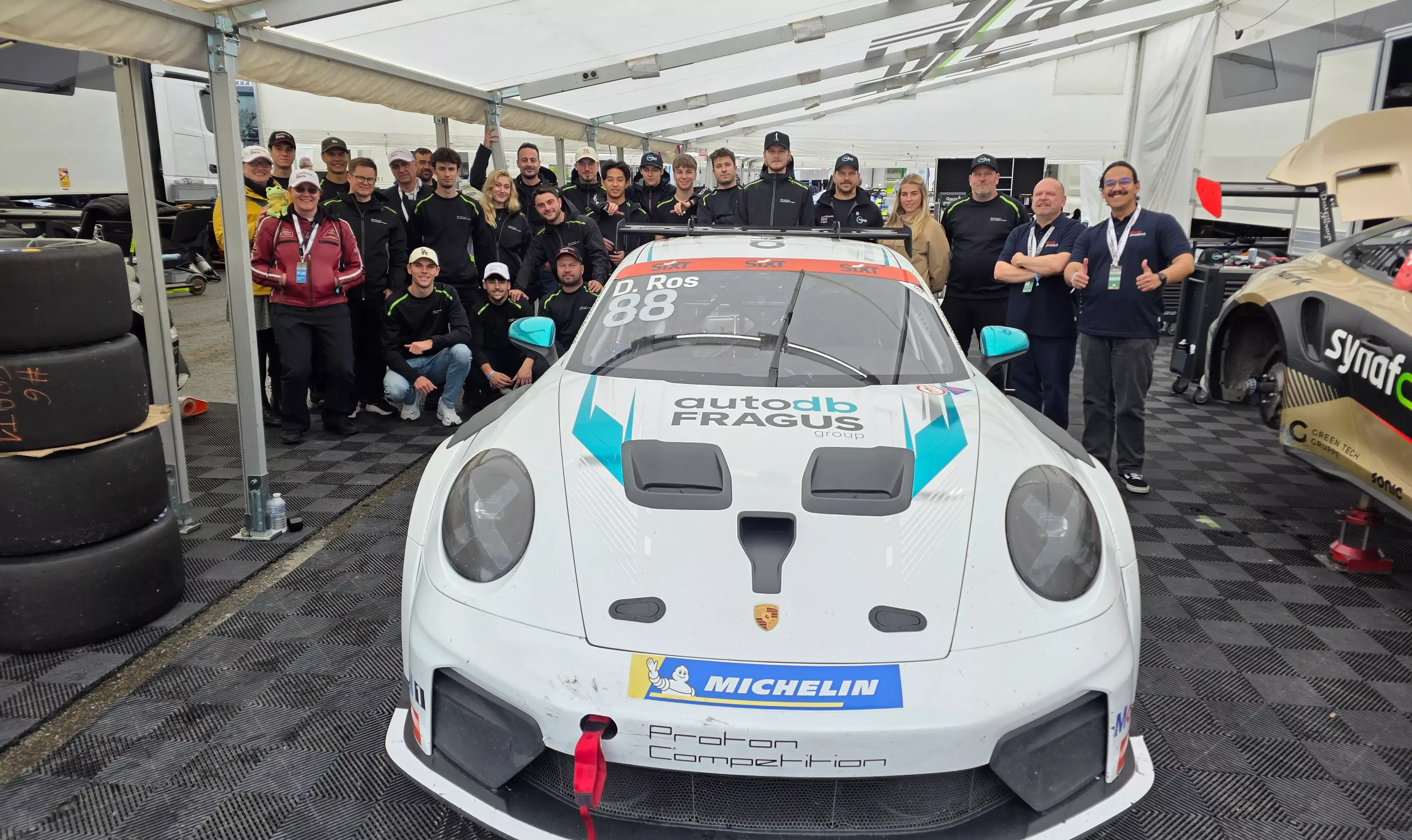 Team von Proton Competition mit Porsche 911 Cup in der Box beim Porsche Carrera Cup Deutschland 2026 zusammen mit Mauricio Schröder und Rajko Matek – beide Mitarbeiter von secura protect (rechts im Bild)