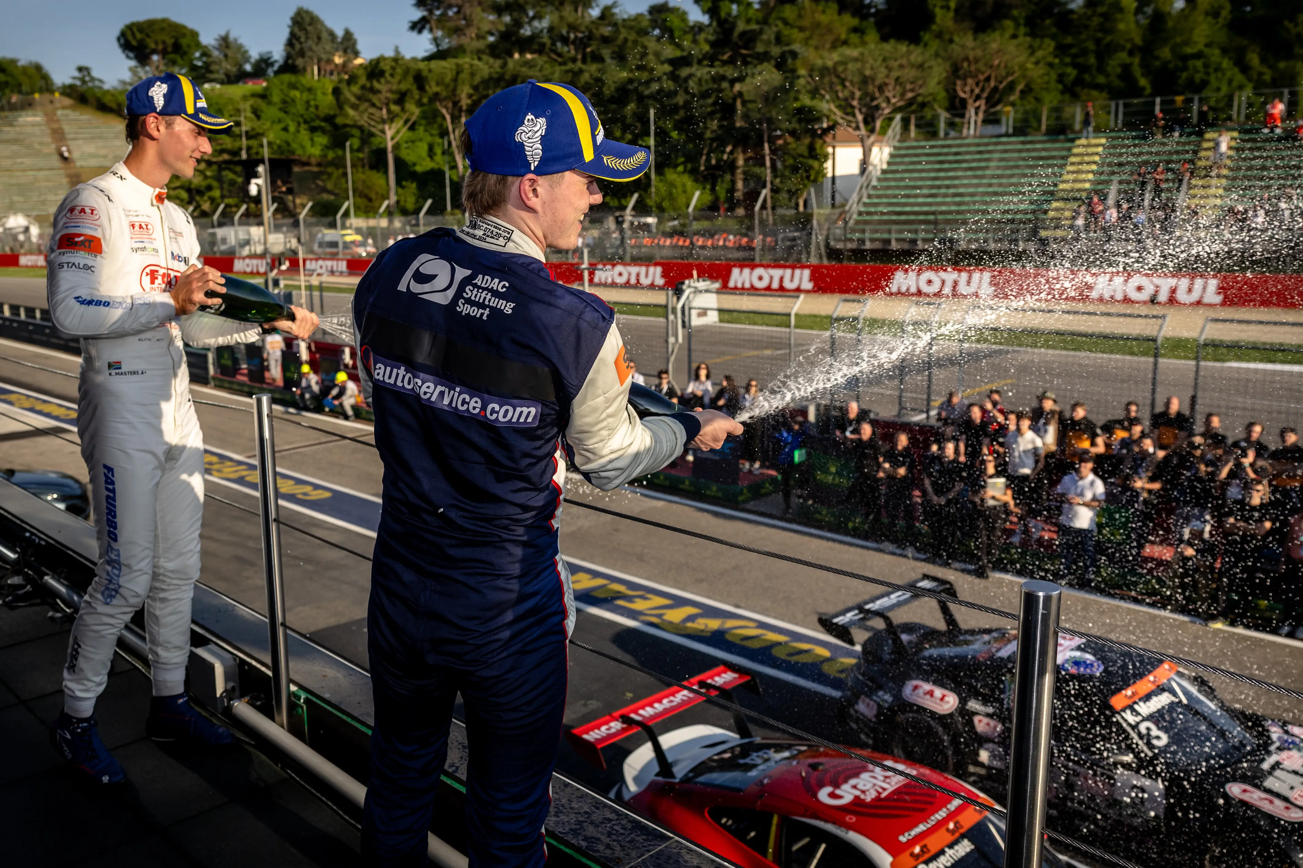 Fahrer von Proton Competition auf dem Podium mit Blick auf die Rennstrecke und auf das Publikum mit Champagner-Taufe